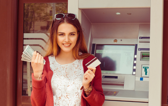 Woman in front of ATM holding cash and card